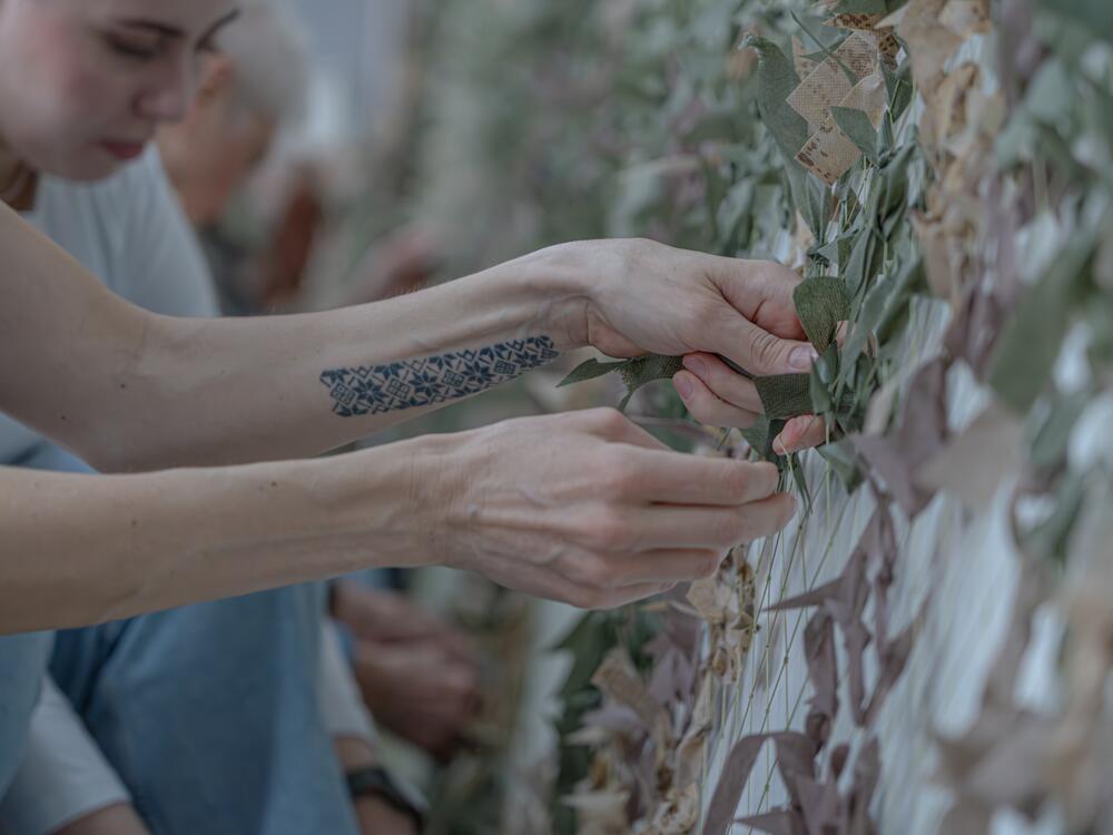 Kateryna Kyshkan weaves strips of cloth into camouflage netting. She worried that her patriotic Ukrainian tattoo would get her arrested at Russian checkpoints.