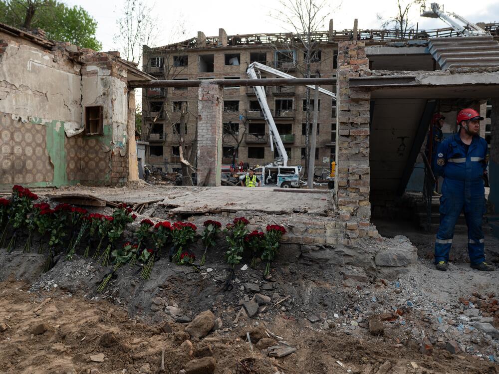 Rescue workers stand near a destroyed building, where roses are placed in Kyiv, Ukraine, in tribute to the victims of the Russian rocket attack the day before, on April 24.