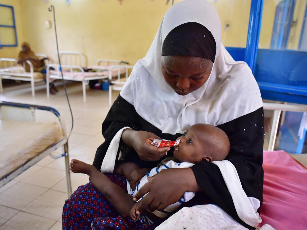 This photo taken on June 14, 2016 shows a woman feeding her child suffering from malnutririon with a pack of 