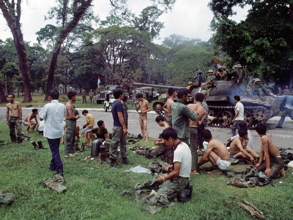 As victorious North Vietnamese troops ride past on a tank, defeated South Vietnamese troops discard their uniforms in Saigon on April 30, 1975, the day the South Vietnamese capital fell to communist forces, ending the Vietnam War.
