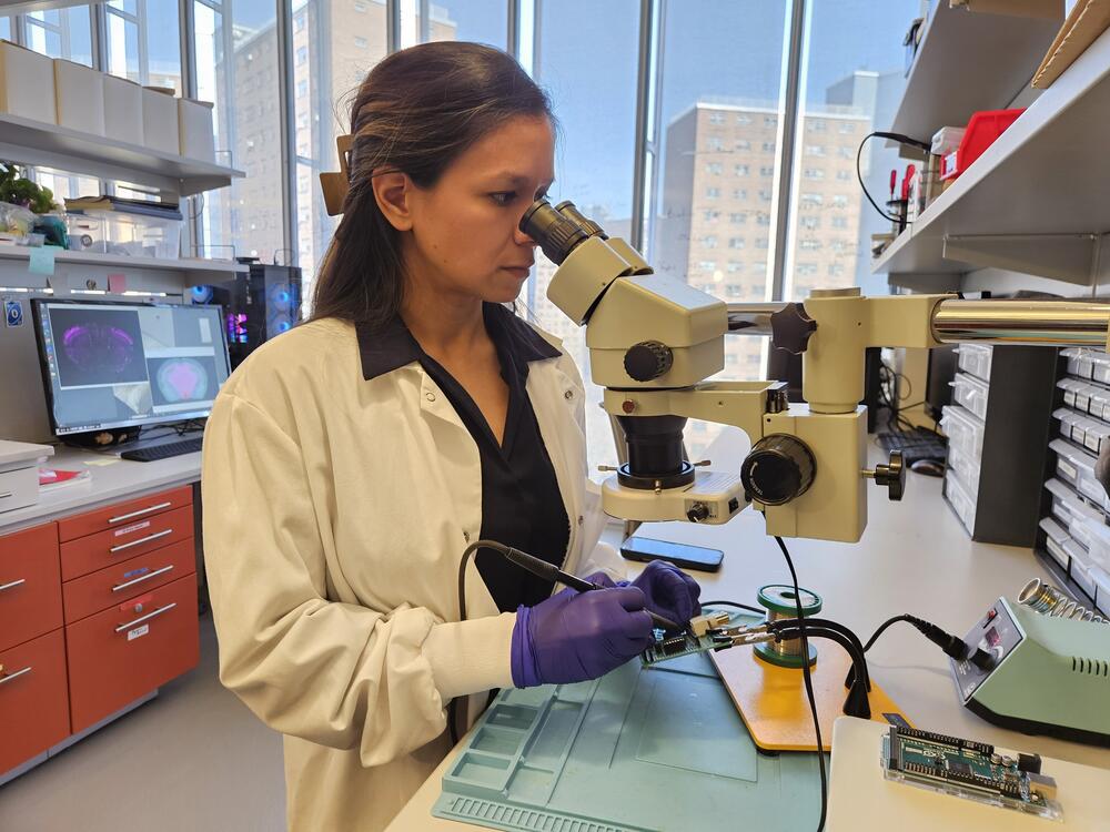 Erica Rodriguez, a scientist and MOSAIC grant awardee at Columbia University, uses a microscope to help her solder a circuit board as part of her brain research. The Trump administration defunded the MOSAIC grant program as part of a purge of diversity-focused initiatives. (Tyler Gibson)