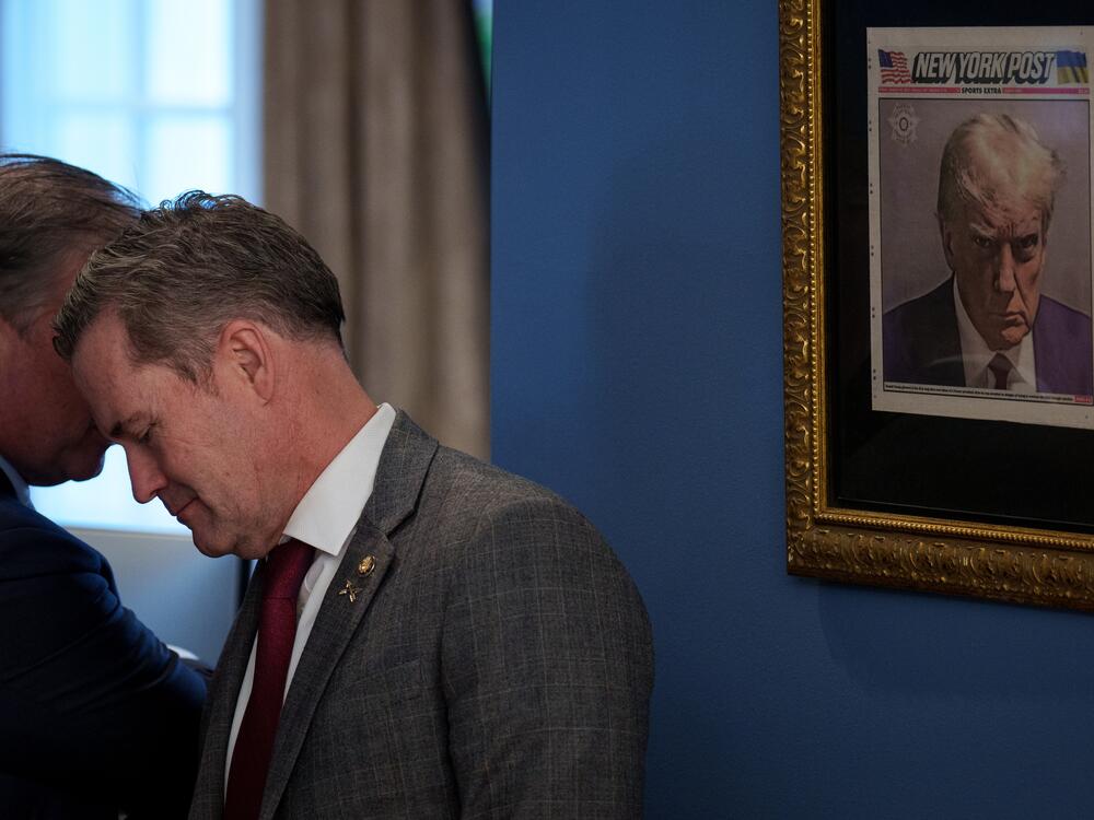In this file photo from Feb. 14, 2025, Mike Waltz speaks with an official just outside the Oval Office where a copy of President Trump's mugshot on the front page of the <em>New York Post</em> is posted.