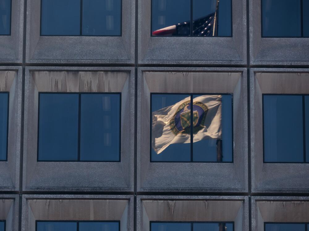 The reflection of the flag of the U.S. Department of Energy is seen on the department's headquarters building in Washington, D.C., in March. The Joint Office of Energy and Transportation, a unique government body designed to bring together expertise from the Department of Energy and the Department of Transportation, has been affected deeply by government-wide efforts to cut jobs. Former staffers say there are no full-time federal employees remaining at the Joint Office.
