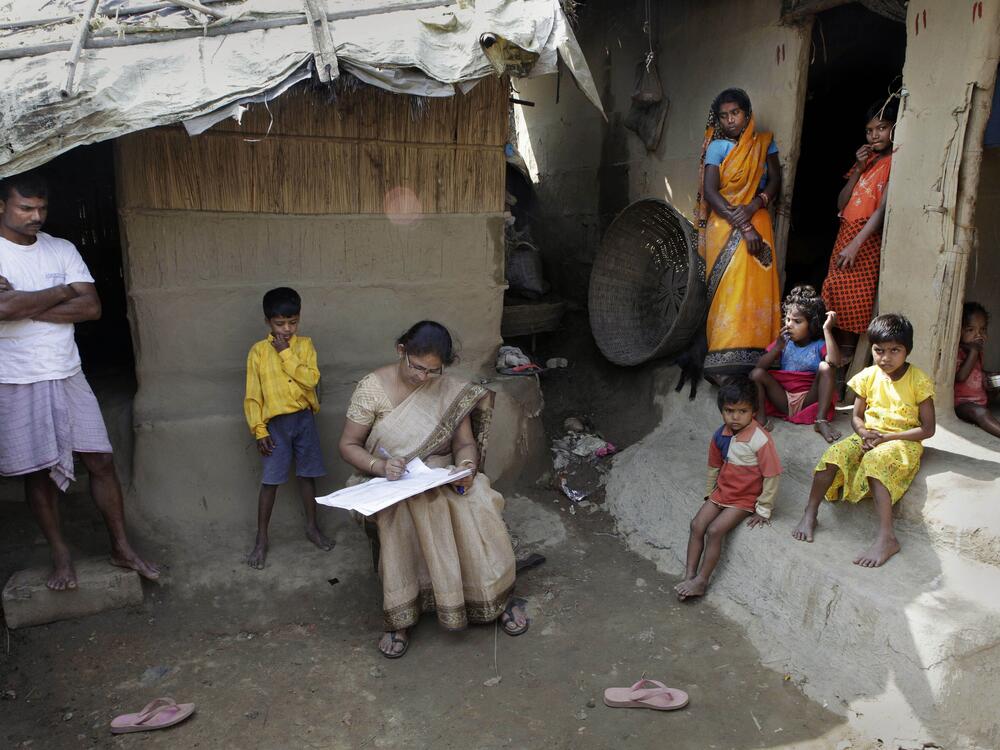 Mahesh Shah, left, stands as his family members look while census worker Rumima Das, writes the information on a paper on the first day of the national census at Ramsingh Chapori village, east of Gauhati, India in 2010.