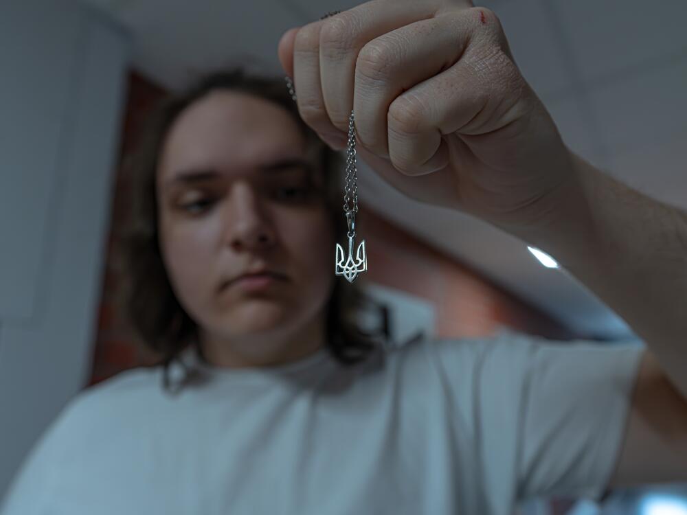 Ivan Sarancha shows Ukraine's coat of arms on a chain in the dormitory for displaced Ukrainians where he's staying. He says for a long time he wanted to buy this type of necklace, which he says could not be worn in occupied Luhansk.