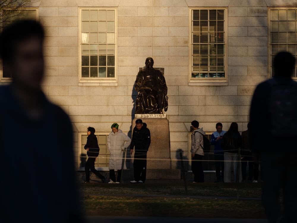 People gather to take photos with the John Harvard statue at Harvard University. President Trump made another threat to Harvard's tax-exempt status in a social media post on Friday.