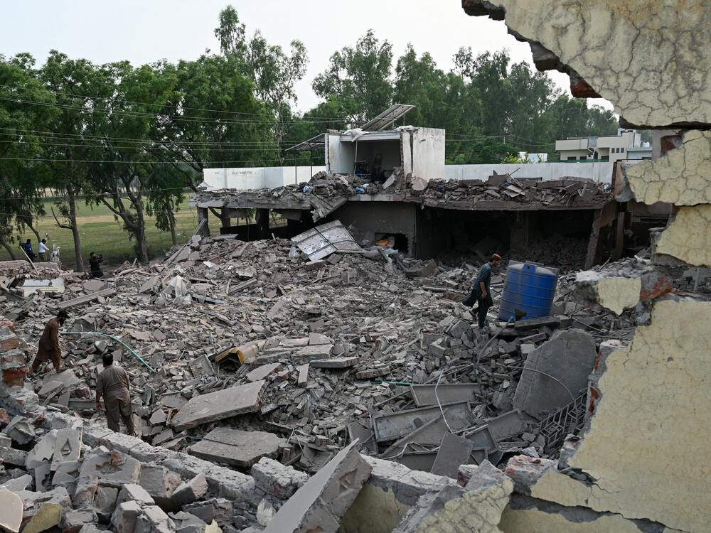 Locals stand on the debris of destroyed structures at a government health and education complex in Muridke, Pakistan, on Wednesday, after Indian strikes.
