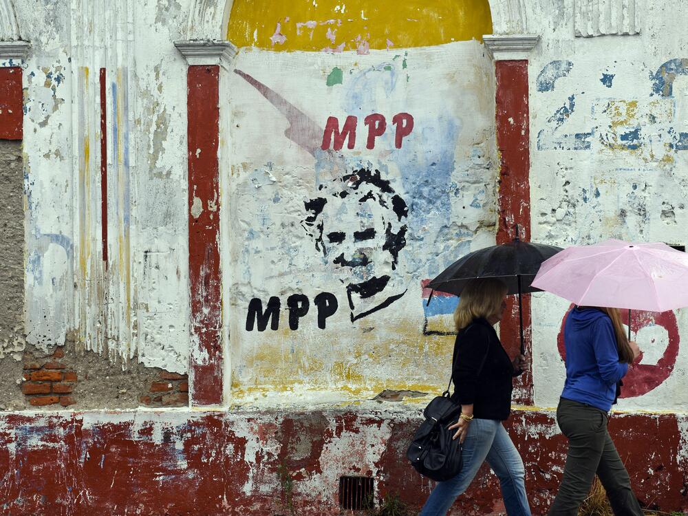 People walking in the rain pass by an image of Uruguay's then-president, José Mujica, during the presidential runoff election in Canelones, Uruguay, on Nov. 30, 2014.