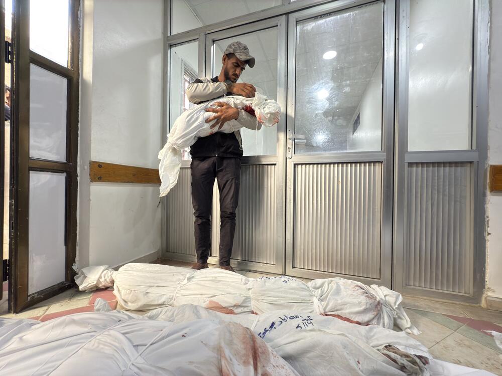 A man holds the body of a child at a hospital morgue in Beit Lahia, Gaza as he stands next to the bodies of other family members killed in Israeli airstrikes in northern Gaza on May 14, 2025.