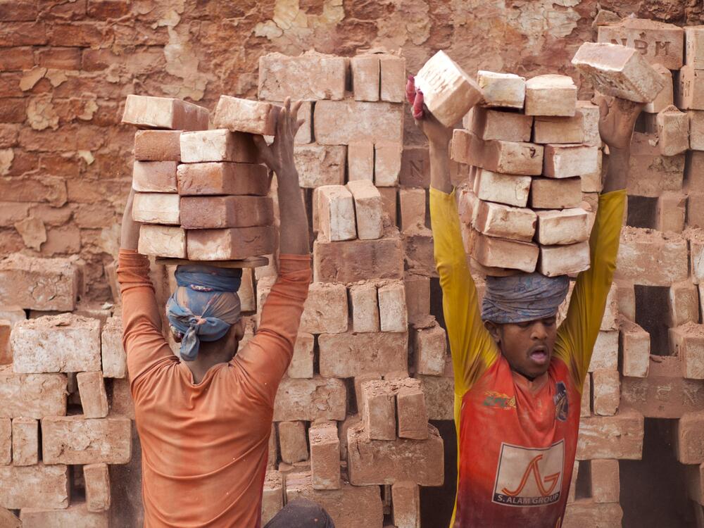Brick workers balance stacks of bricks on their heads as the carry them from the kiln near Dhaka, Bangladesh.