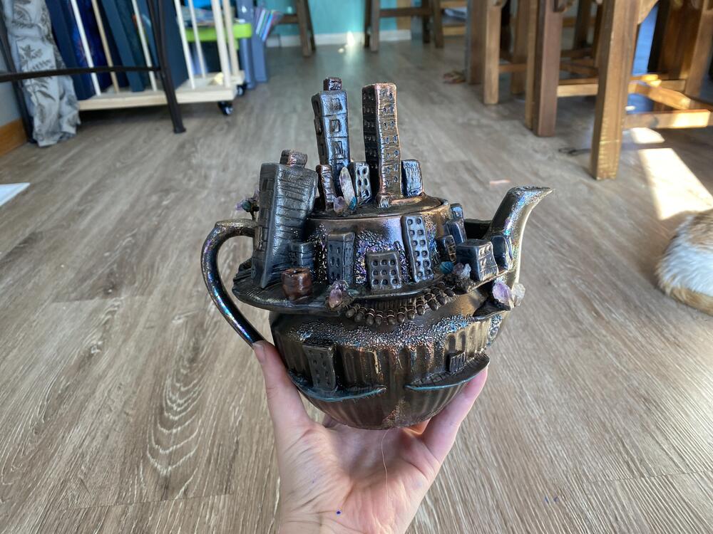 Ashley Voortman shows off a teapot she made with a tiny abandoned city on it.