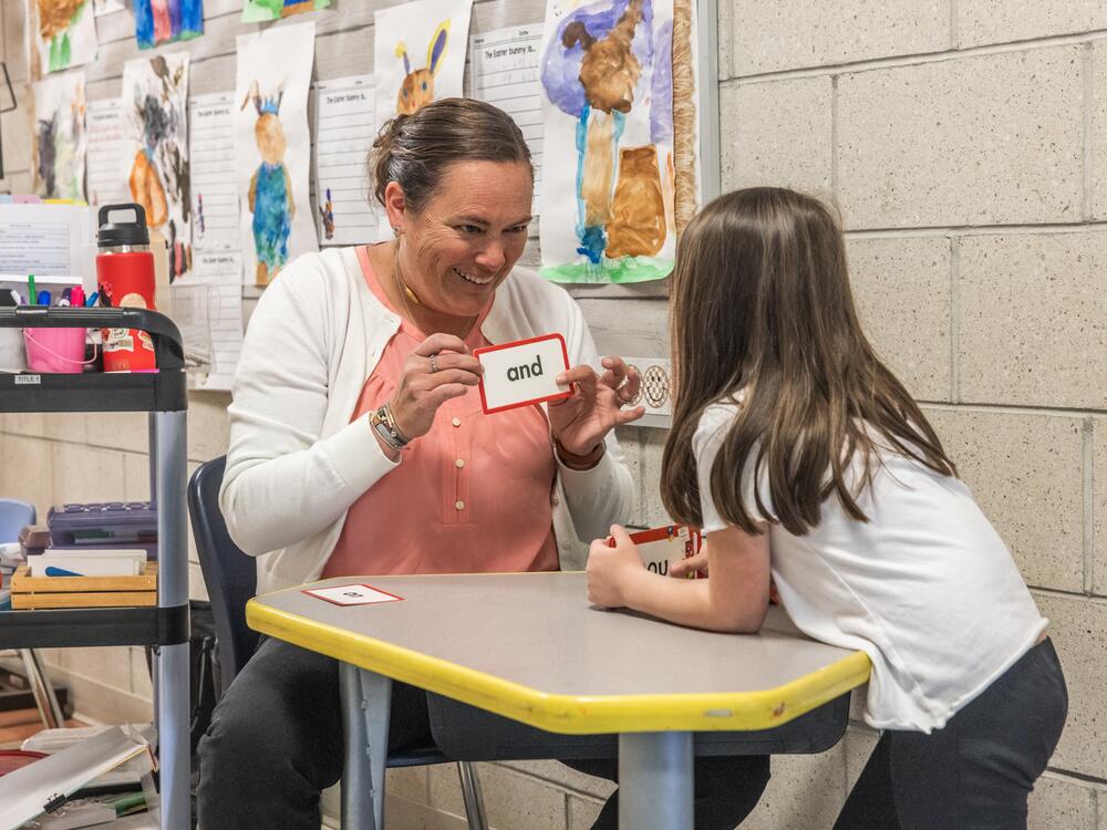 Teaching assistant Nicki Longyear works one-on-one with a kindergartener in the hallway outside a classroom at Mill Stream Elementary School.