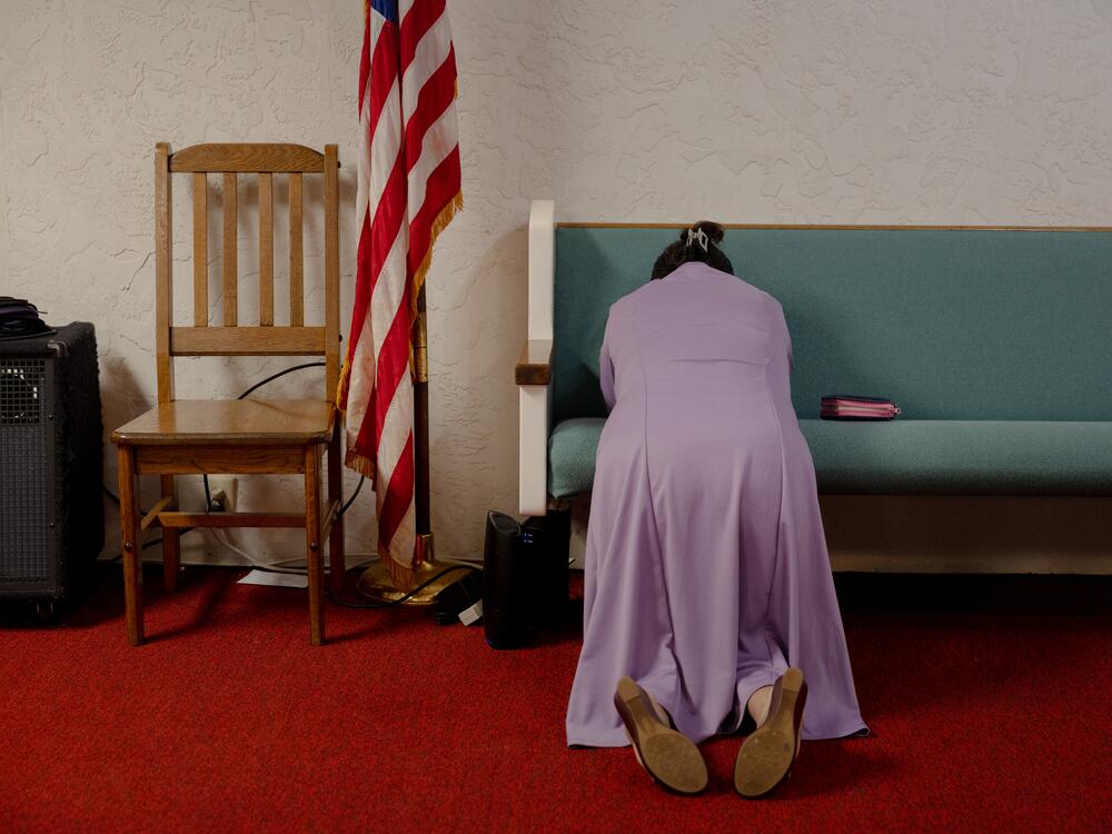 M. prays next to a U.S. flag during church service, Sunday, May 11, 2025, in Tampa, Florida. M., Maurilio's wife, continues to have faith that he will return home, although the family is preparing for a worst-case scenario.