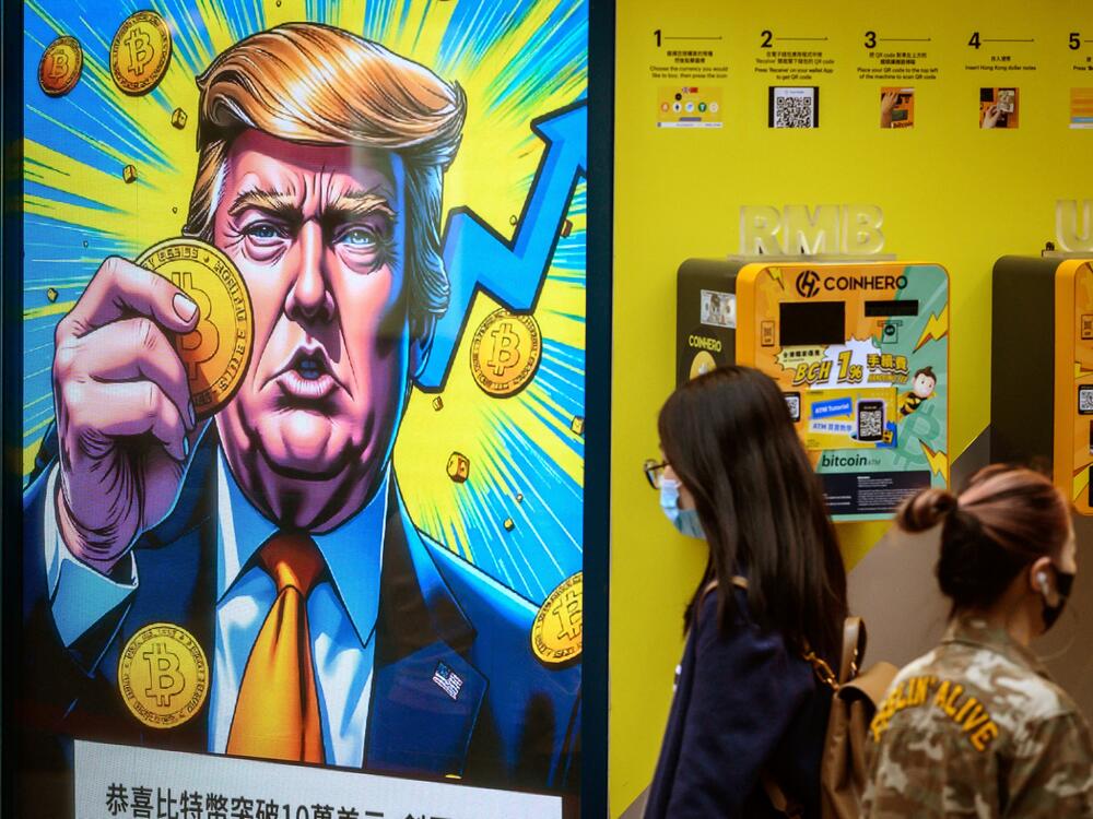 People walk past a cryptocurrency exchange office with a screen featuring President Donald Trump holding cryptocurrency coins in Hong Kong on March 12, 2025.