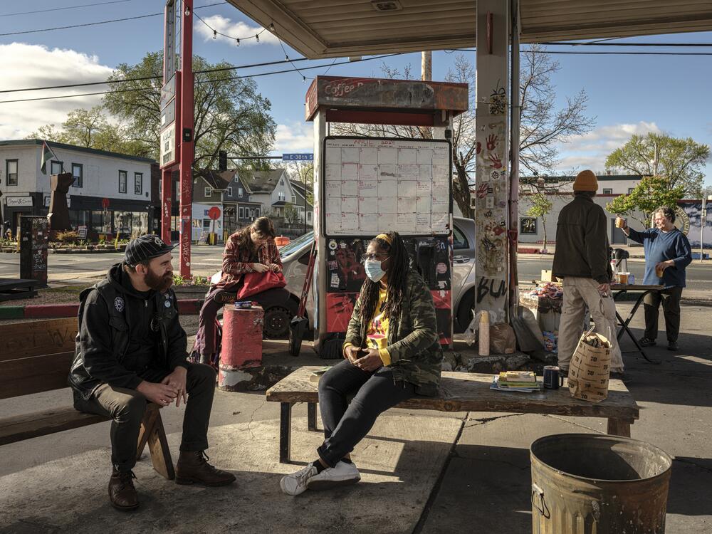 Marcia Howard, seated at center, speaks with another community member at George Floyd Square. Activists say they have gathered here every morning for the last five years.