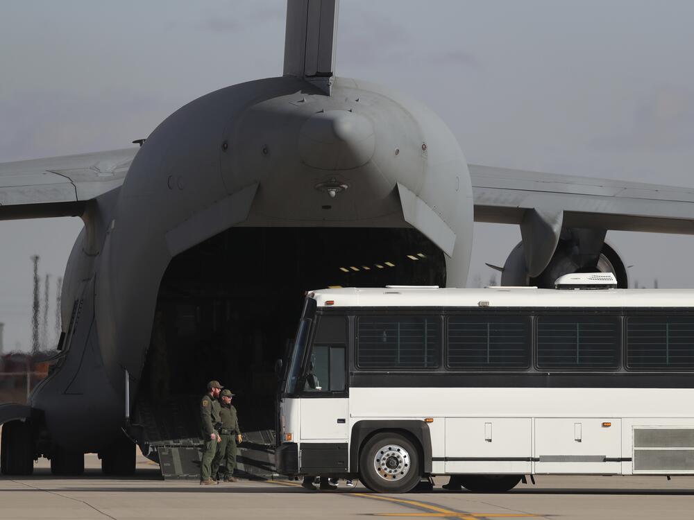 A military aircraft waits for migrants to board from a bus at Fort Bliss in El Paso, Tx., on Jan. 30, 2025, before deporting them to Guatemala.