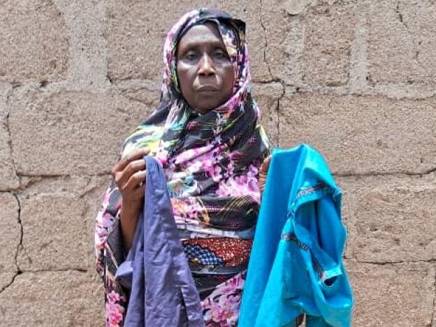 Mariam Mohammed, a widow, stands outside her home in Bama, Nigeria. She's holding her younger son Babagana's favorite clothes. He died in early February from complications of sickle cell disease. She had taken him to a U.S.-funded clinic for treatment, but at that time the facility was shuttered due to a stop-work order issued by the Trump administration.