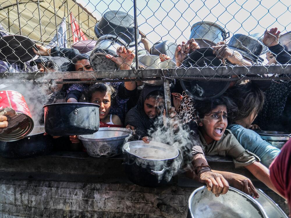 Displaced Palestinians, including women and children living in tents, receive food distributed by aid organizations in al-Mawasi district of Khan Younis, Gaza, on May 30. In Jordan, tens of thousands of boxes of food aid for Gaza are moldering in warehouses.