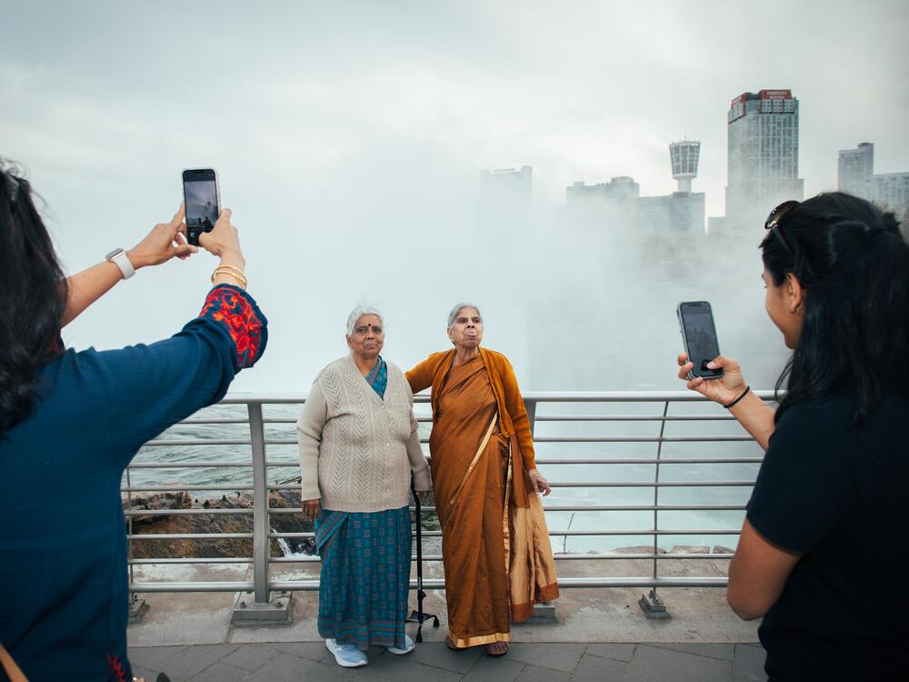 Two grandmothers pose in front of Niagara Falls while their daughter and granddaughter take their photo on May 12, 2023.