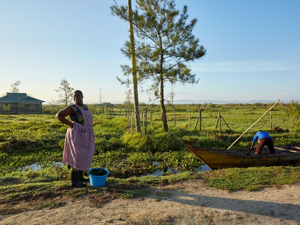 Alice Akinyi, a No Sex For Fish member, waits to take a boat to Nduru Beach to get the latest catch from the fishermen to sell — roads were damaged by past floods so it's hard to get to the shore these days. She's one of only two members whose fishing boats are still functioning. The lower half of the house behind her — the area that's darker — was underwater during the peak of the flooding. The structure is no longer habitable.