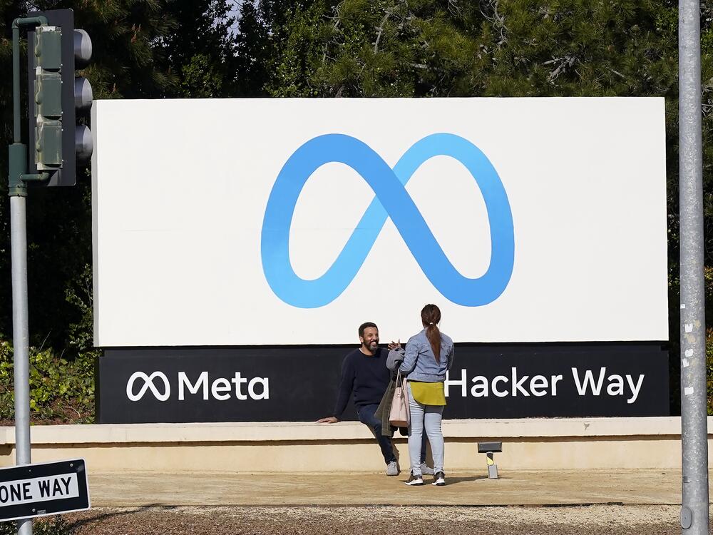 People talk near a Meta sign outside of the company's headquarters in Menlo Park, Calif.