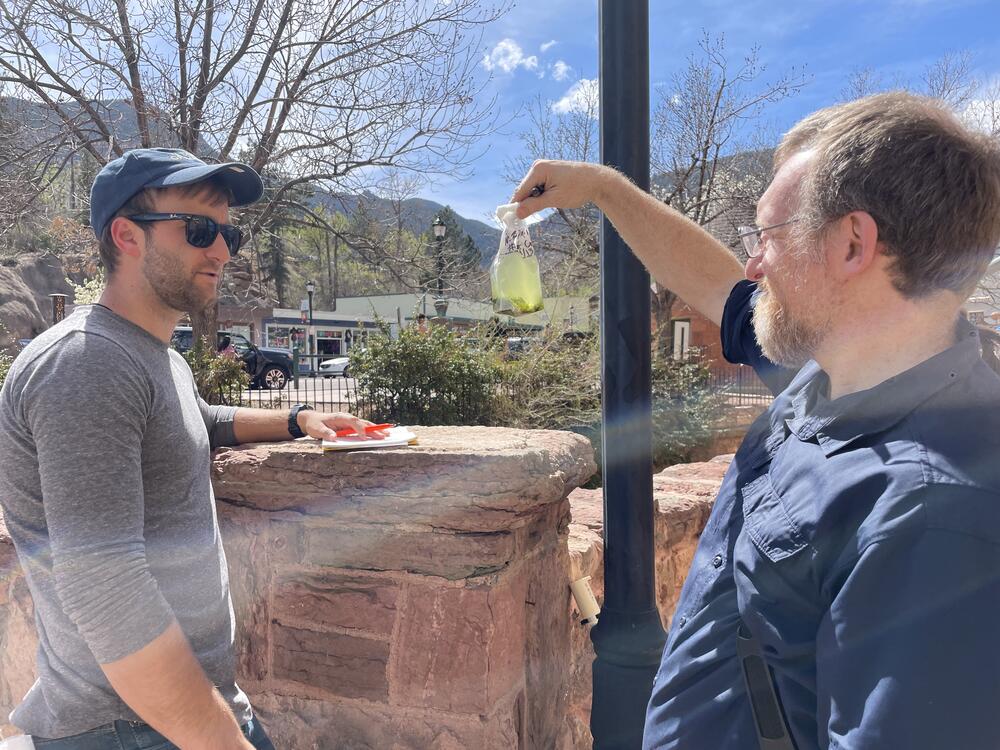 James Henriksen with Colorado State University holds up a water sample for Harvard colleague Braden Tierney. The bag is teeming with microbes that they hope may help solve some of humanity's big problems.