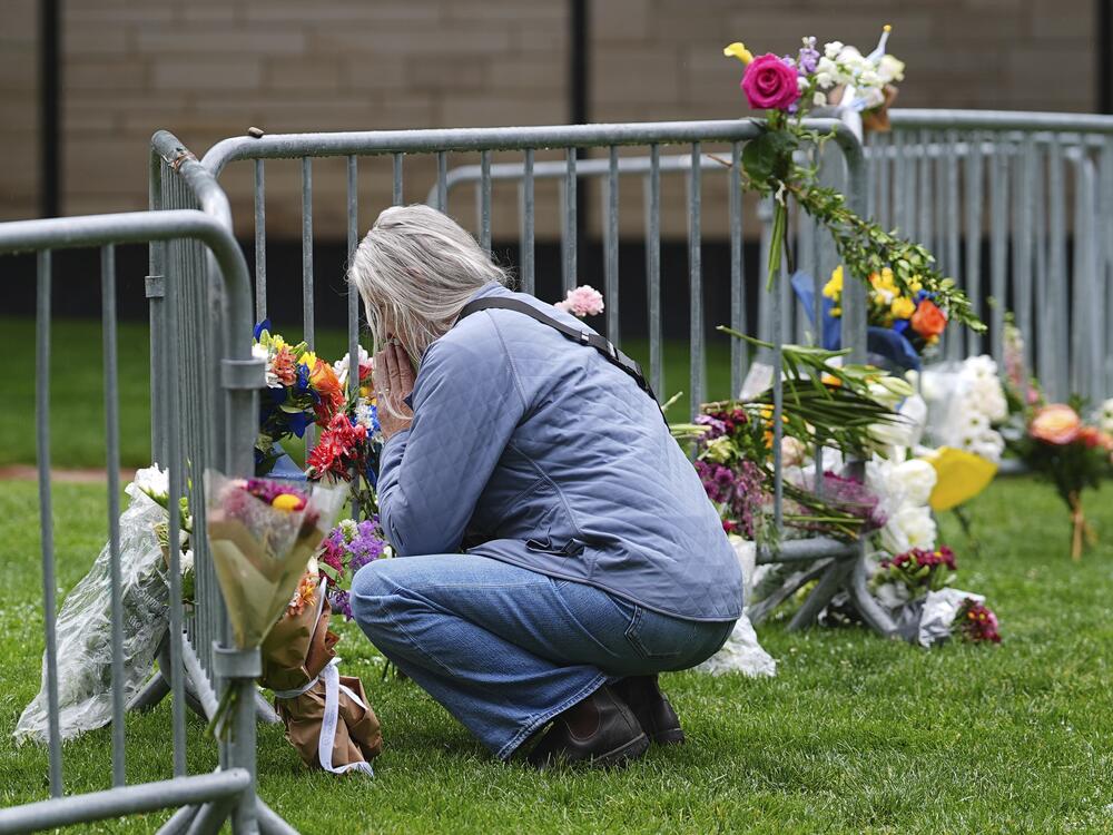 A visitor offers a tribute after leaving a bouquet of flowers at a makeshift memorial for victims of an attack outside of the Boulder County, Colo., courthouse as a light rain falls Tuesday, June 3, 2025, in Boulder, Colo. (AP Photo/David Zalubowski)