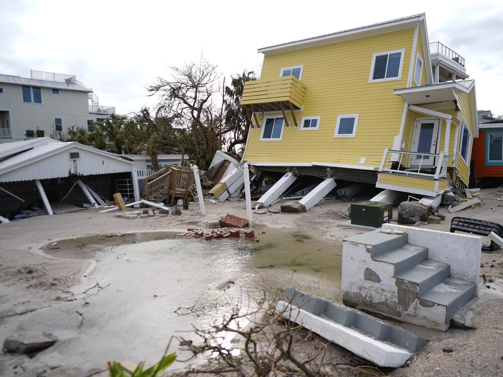 A house, center, lies toppled off its stilts after the passage of Hurricane Milton, alongside an empty lot where a home was swept away by Hurricane Helene, in Bradenton Beach on Anna Maria Island, Fla.