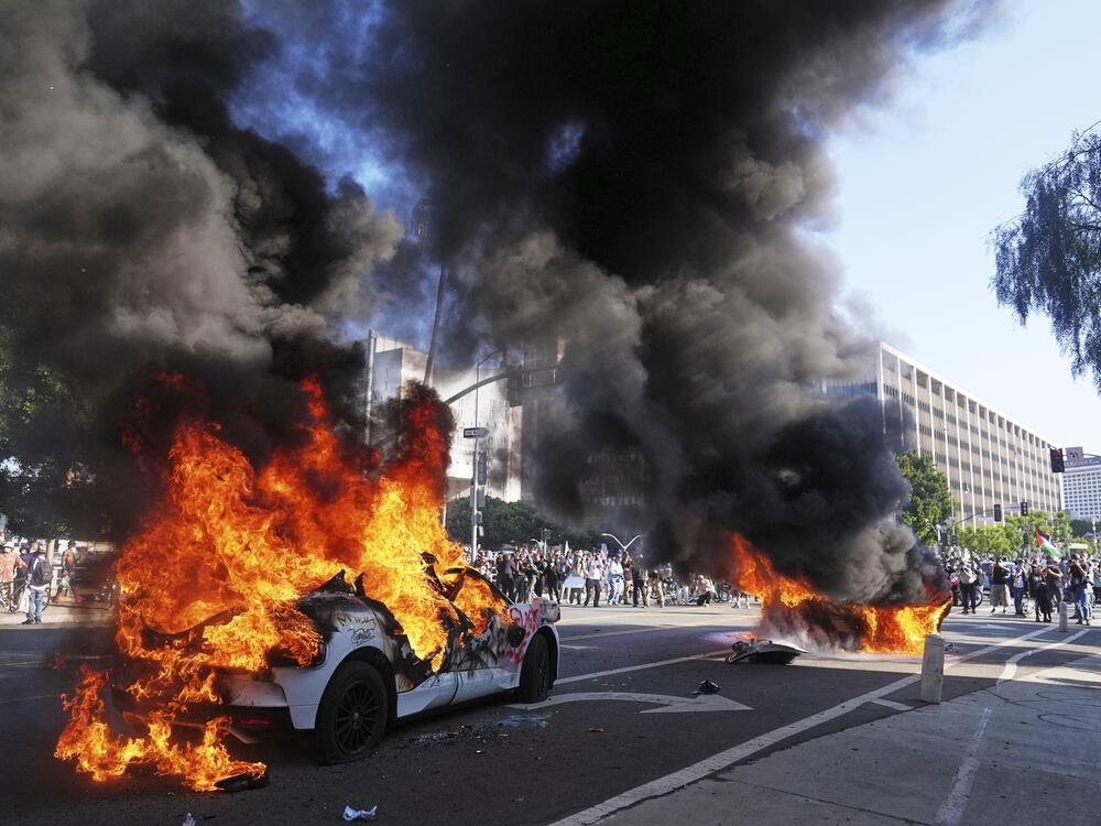 Two Waymo taxis burn near the metropolitan detention center of downtown Los Angeles, Sunday, June 8, 2025, following last night's immigration raid protest.<br>