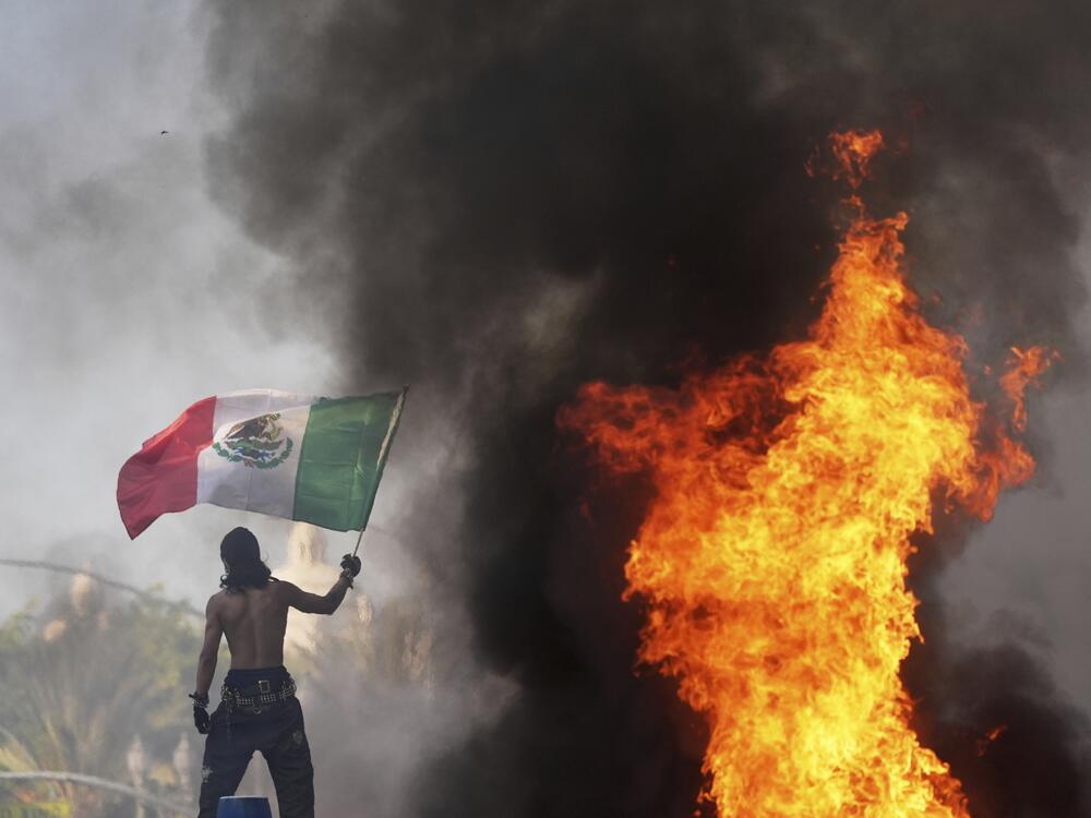 A protester waves a flag as a Waymo taxi burns near the Metropolitan Detention Center of downtown Los Angeles.