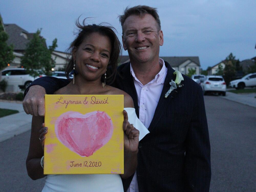 Lynnea and David Hutton embrace and smile as they pose for the photo with a sign showing their wedding date.
