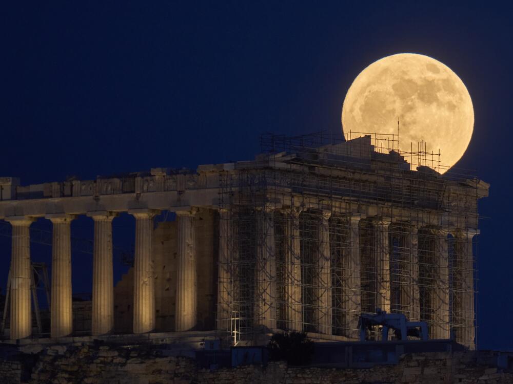 The strawberry Moon rises in the sky behind the 5th century B.C. Parthenon temple at the ancient Acropolis hill, in Athens, Greece.