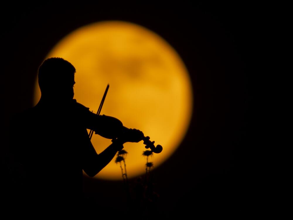 A person plays the violin as the full moon appears over Halabja, Iraq on June 10, 2025.