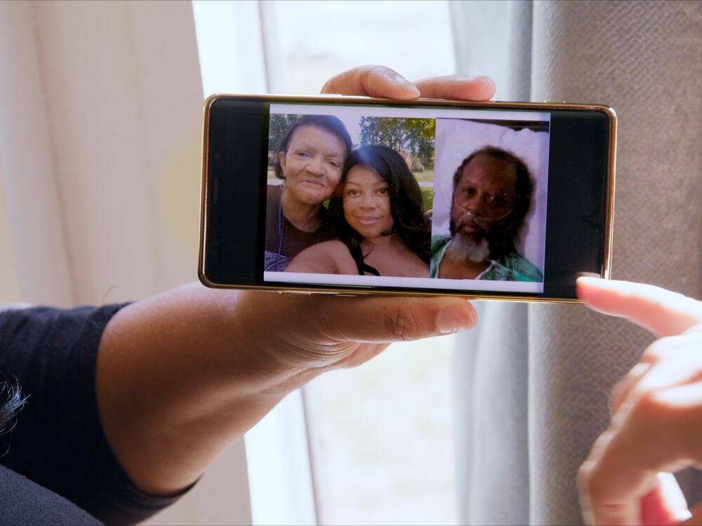 Shalana Jordan holds a photo of her and her parents, Nola and Robert Ramsuer, displayed on her phone.