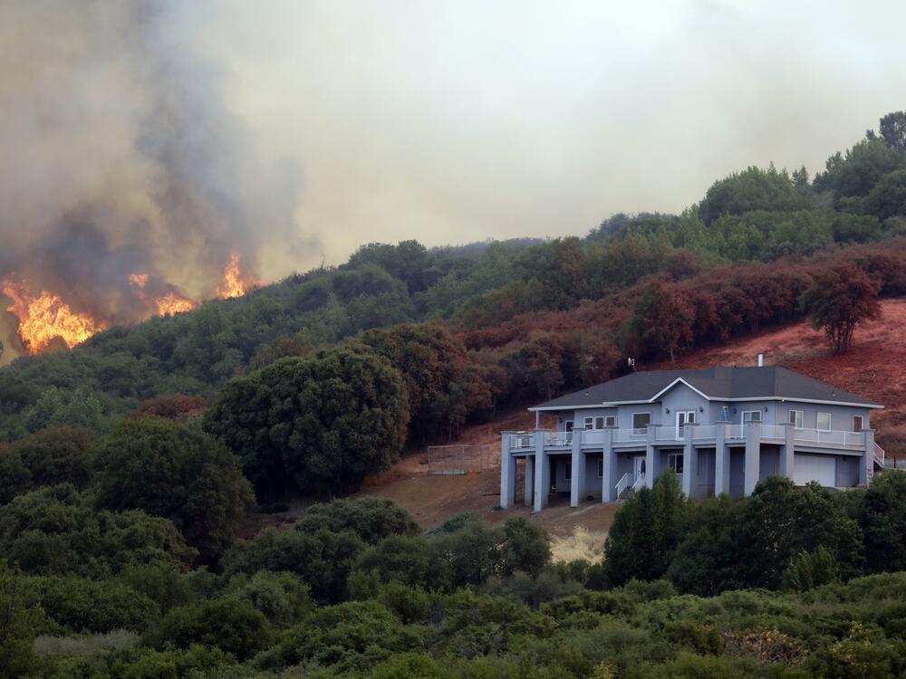A wildfire crests over a ridge, threatening a home in Lake County, Calif., in July 2018.