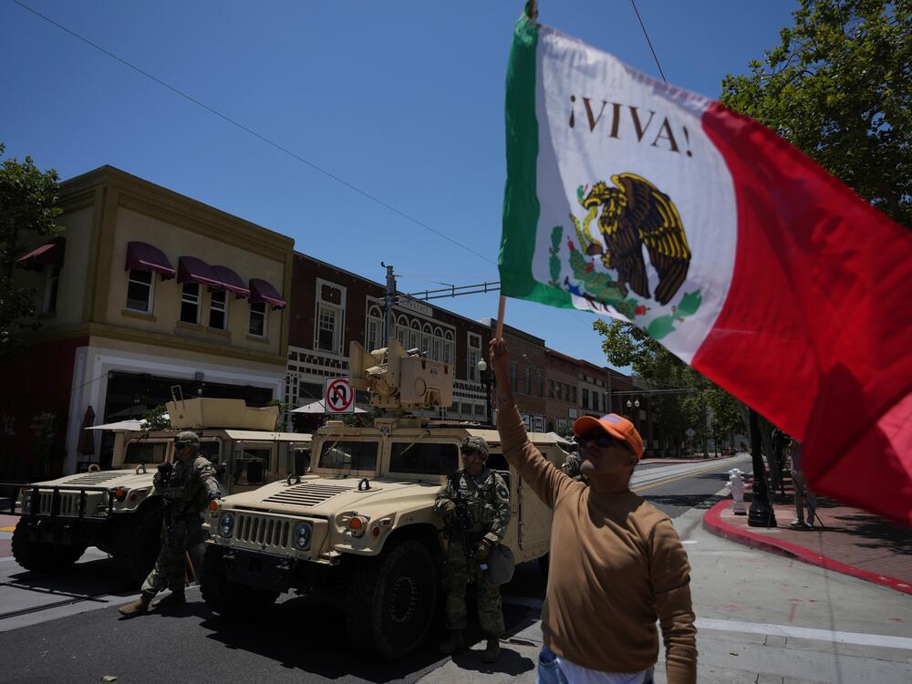 A protester waves a flag standing by California National Guard parked along a street in Santa Ana, Calif. on Tuesday, June 10, 2025.