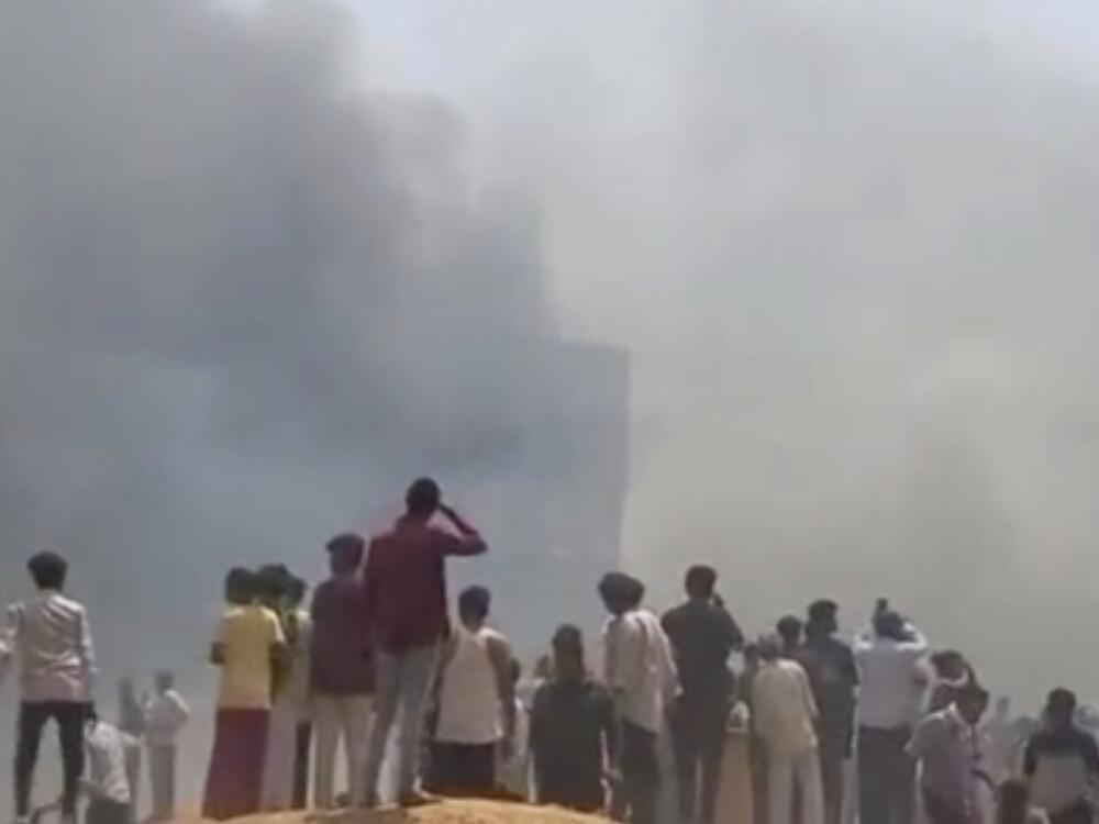People watch smoke rising after an airplane crashed in Ahmedabad, Gujarat state, India, on Thursday.