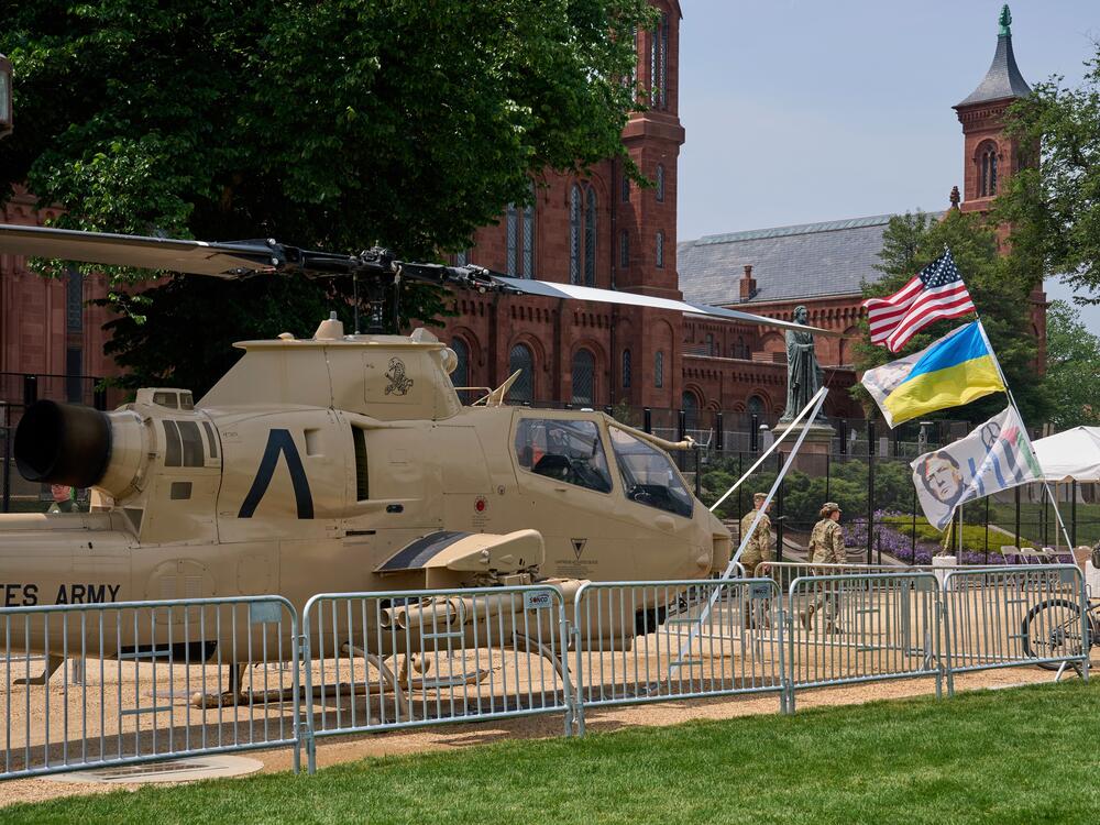 A man bicycles with several flags past a helicopter on display during preparations for an upcoming military parade commemorating the Army's 250th anniversary and coinciding with President Donald Trump's 79th birthday.