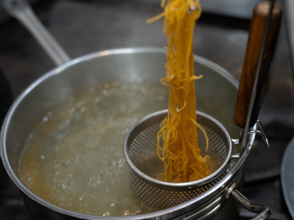 Chef Shuai Wang strains the wonton noodles for the crispy smoked duck dish. 