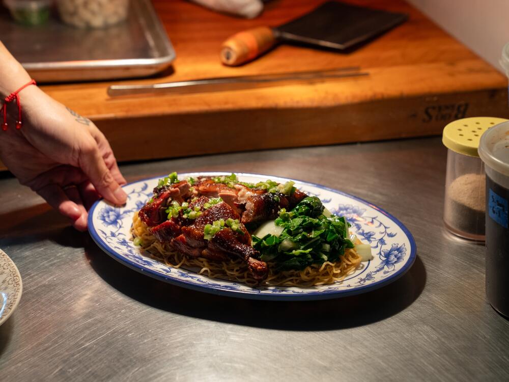 Chef Shuai Wang finishes preparing a dish of crispy, smoked duck on top of noodles with blanched bok choy.
