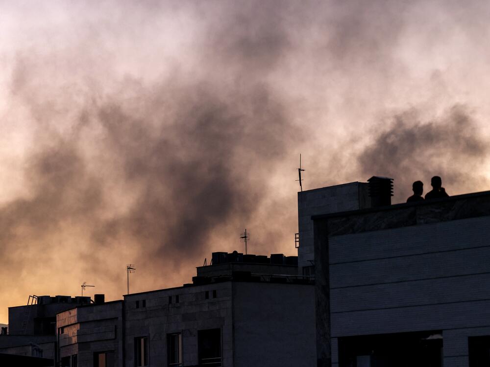 People stand on a rooftop amidst billowing smoke following an overinght Israeli strike in Tehran on June 17, 2025.