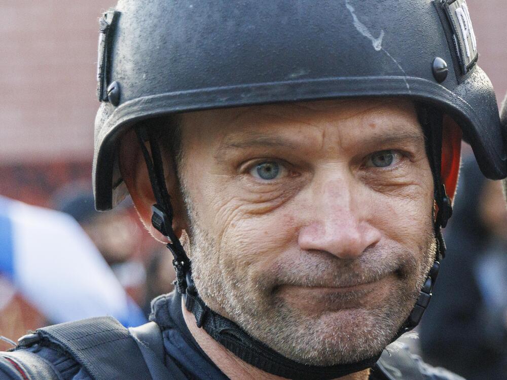 Freelance visual journalist Michael Nigro, shown here at protests in Los Angeles' Koreatown neighborhood shortly after being struck in the helmet by a non-lethal bullet fired by a Los Angeles Police Department officer. His helmet bears a bright mark where the projectile hit him. Given he wears several labels marked 