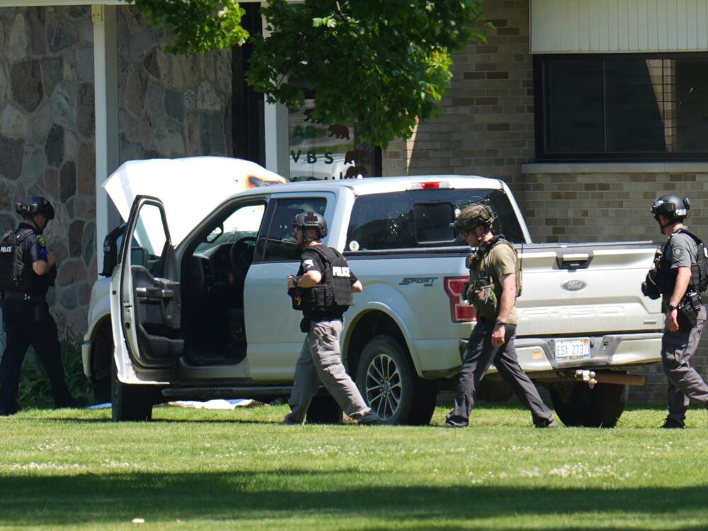 Police walk by an idle vehicle near CrossPointe Community Church in Wayne, Mich., Sunday, June 23, 2025.