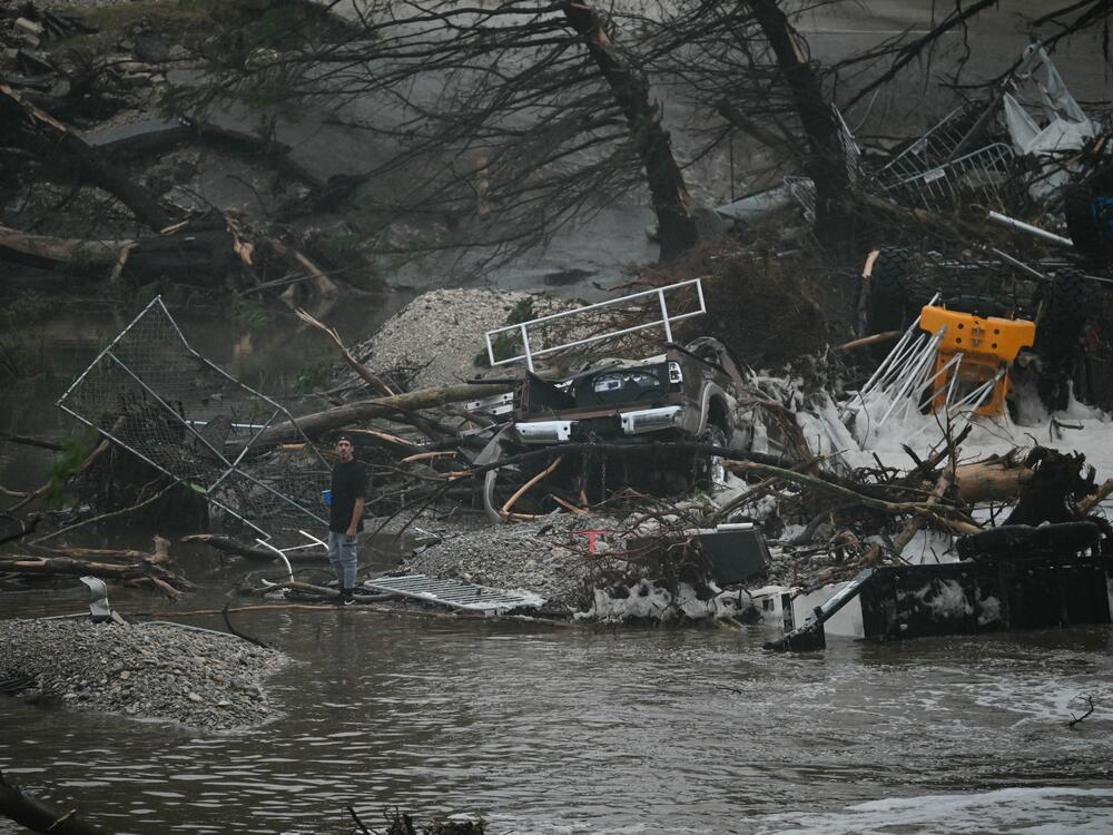 A member of the public stands next to overturned vehicles and broken trees on Saturday after a flash flood at the Guadalupe River in Kerrville, Texas.