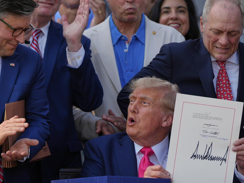 President Trump signs his massive bill of tax breaks and spending cuts at the White House on July 4 in Washington, surrounded by members of Congress.