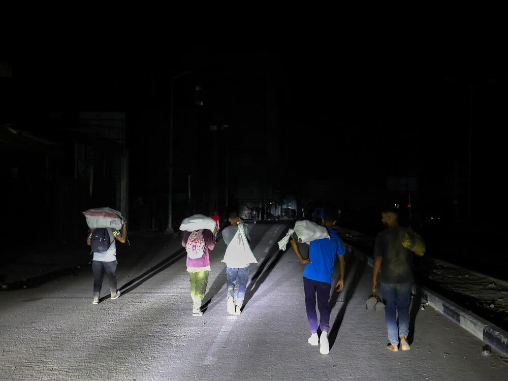 Palestinians walk back, carrying parcels collected from a food aid distribution point set up by the privately run Gaza Humanitarian Foundation (GHF) on the Salaheddin road, at the Nuseirat refugee camp in the central Gaza Strip on June 24, 2025.
