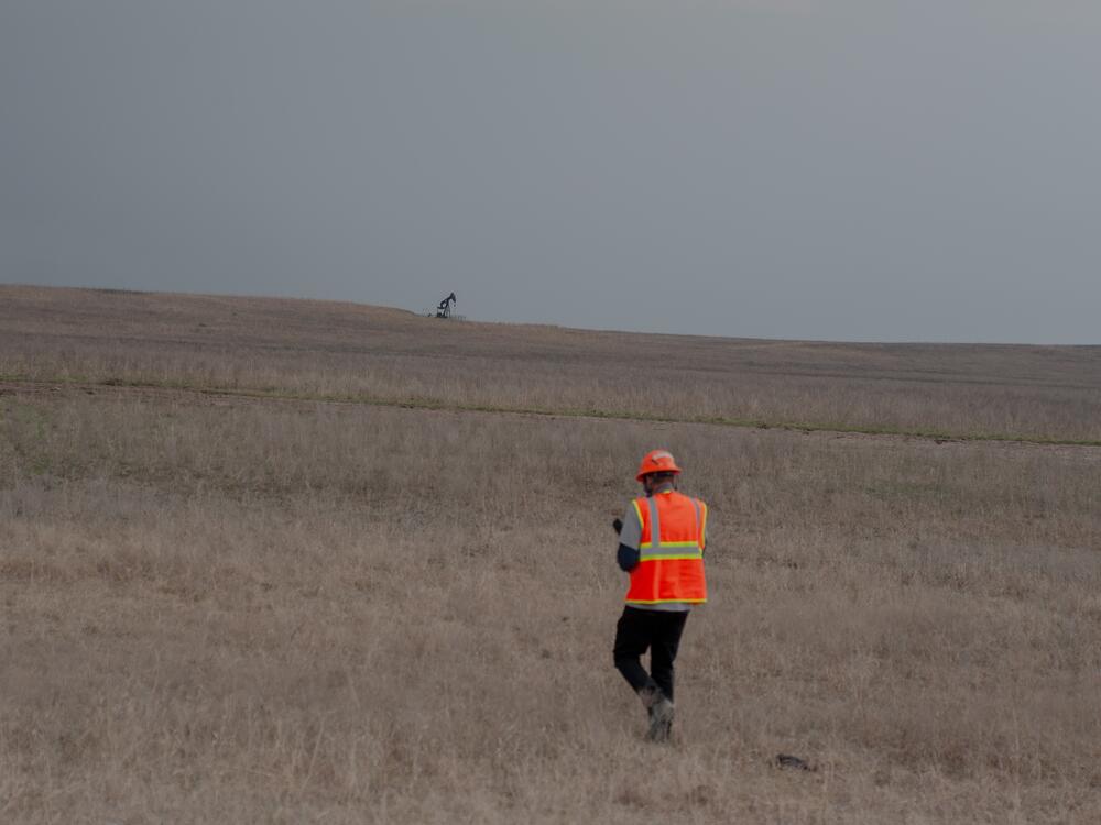 Caldwell walks through dry grass in the Tallgrass Prairie Preserve in Oklahoma on March 20, 2024. A pumpjack is visible in the distance.