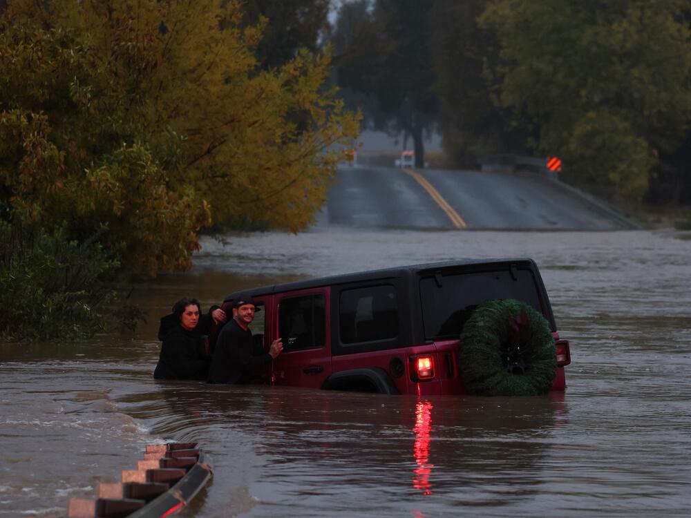 A couple waits for a rescue crew after their car got stuck in deep floodwaters in Windsor, Calif., in November 2024. Experts say you should break your window and climb out as quickly as possible.