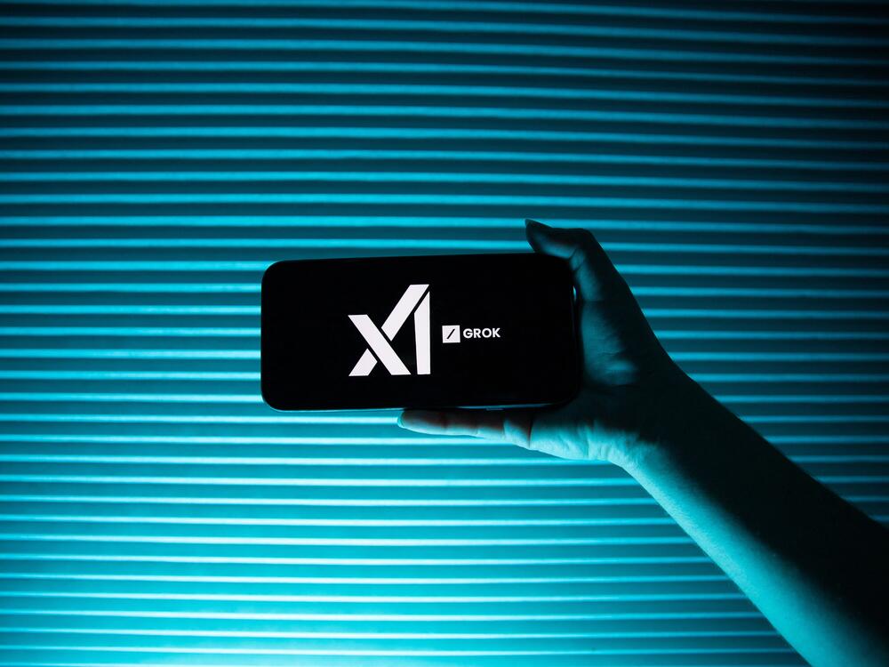 A person holds a telephone displaying the logo of Elon Musk's artificial intelligence company, xAI  and its chatbot, Grok.