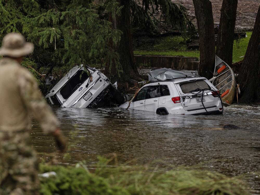 Vehicles sit submerged as a search and rescue worker looks through debris from the early July flash flooding in Hunt, Texas.